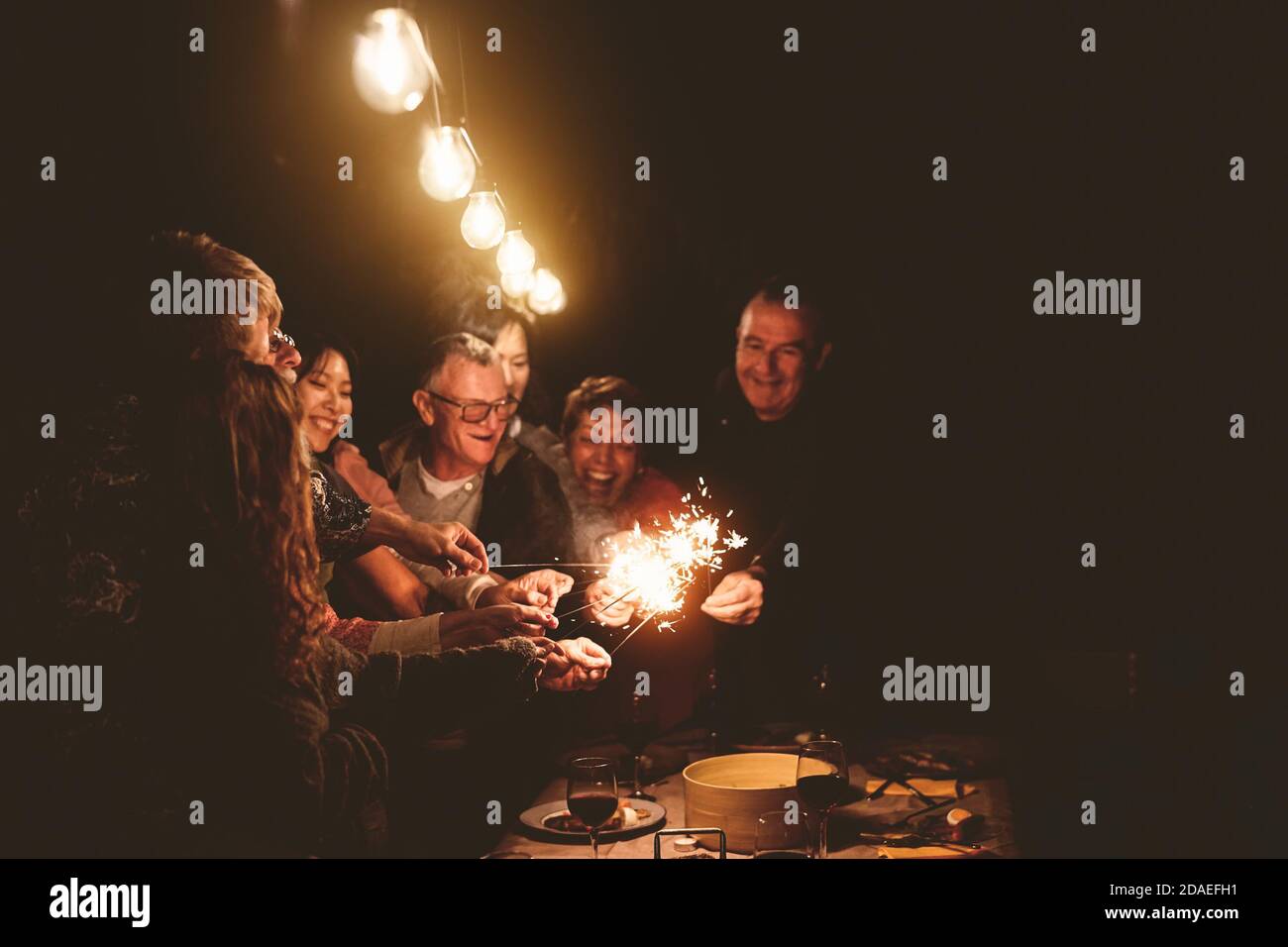 Happy family celebrating holidays with sparklers fireworks at night dinner party - Group of people with different ages and ethnicity having fun Stock Photo