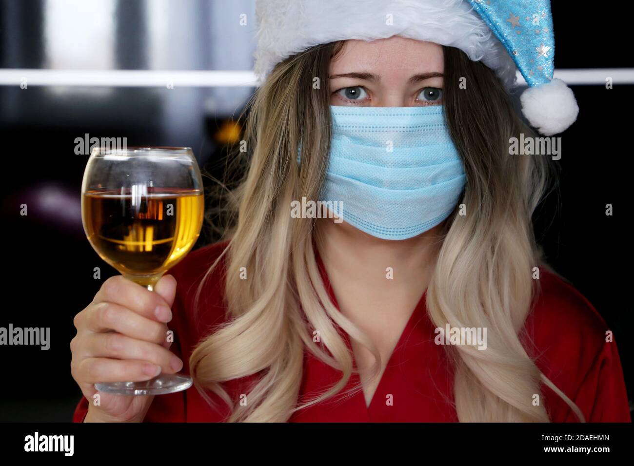 Woman in medical face mask and Santa Claus hat with glass of wine in hand. Christmas celebration during coronavirus pandemic Stock Photo