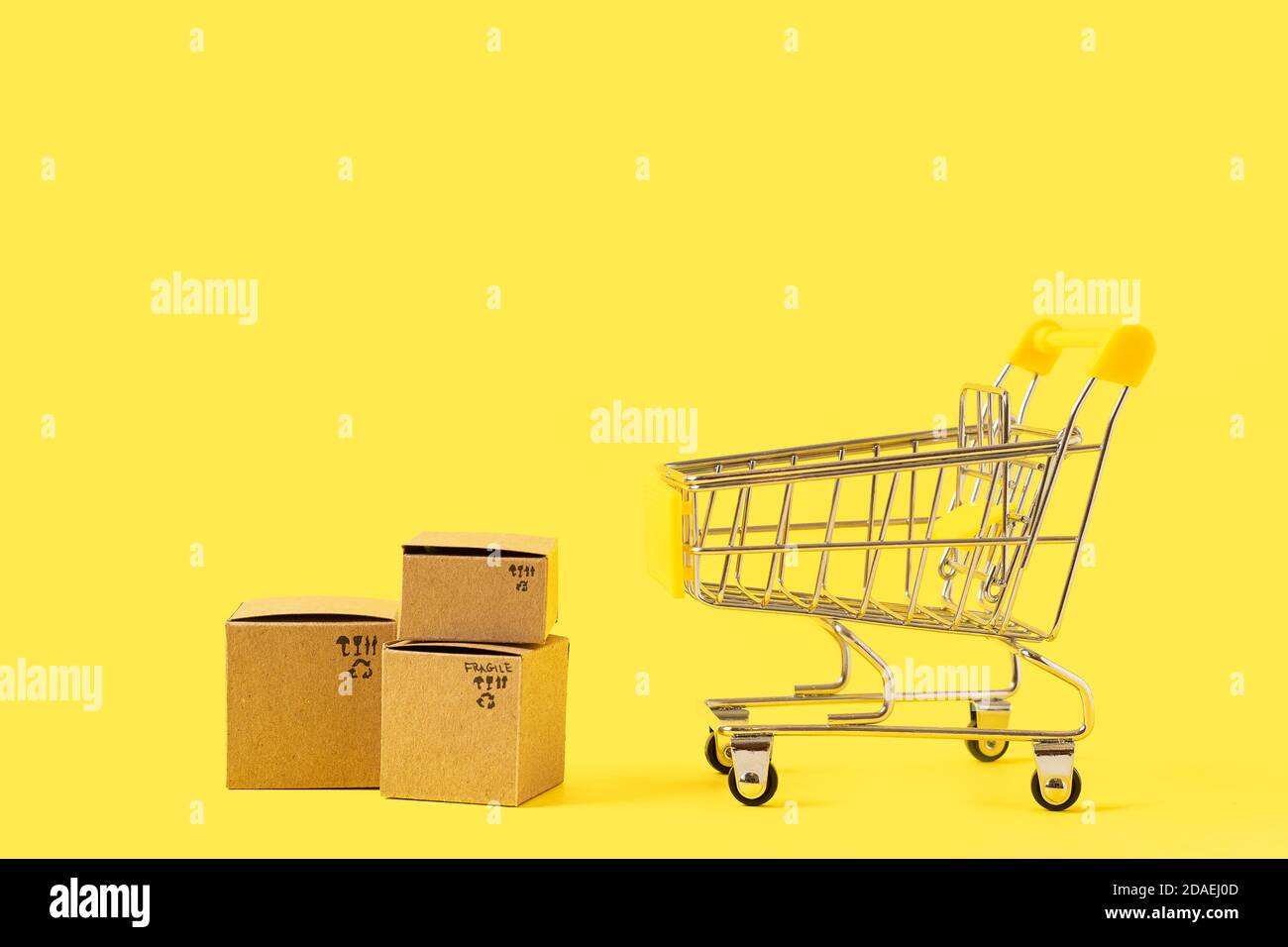 Toy shopping cart with boxes on yellow background. Copy space for text or design. Sale, discount, shopping and delivery concept. Consumer society tren Stock Photo