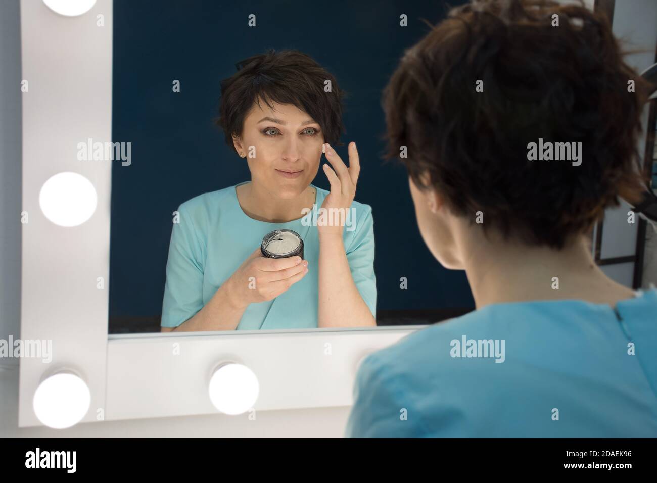 reflection in the mirror of a woman who applies cream on her face Stock Photo