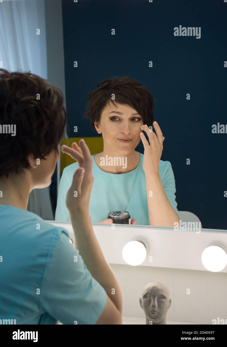 reflection in the mirror of a woman who applies cream on her face Stock Photo