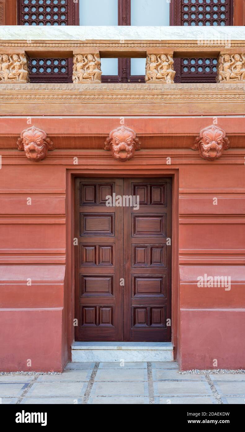 Recessed engraved closed wooden door installed in ornamental stone wall outside of old building with decorated balustrade above Stock Photo