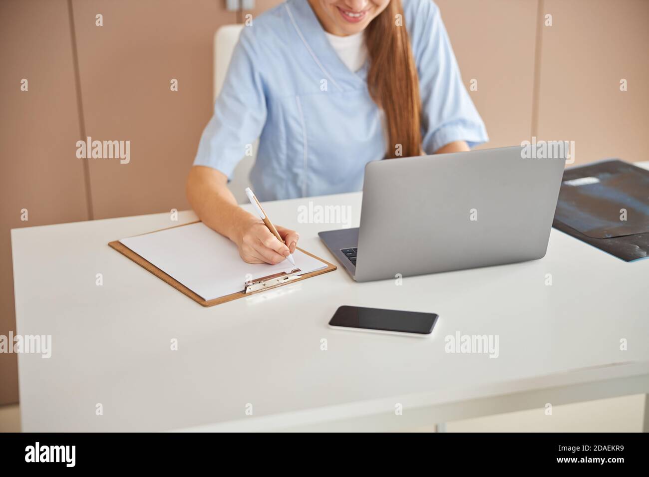 Qualified female doctor writing notes and smiling Stock Photo - Alamy