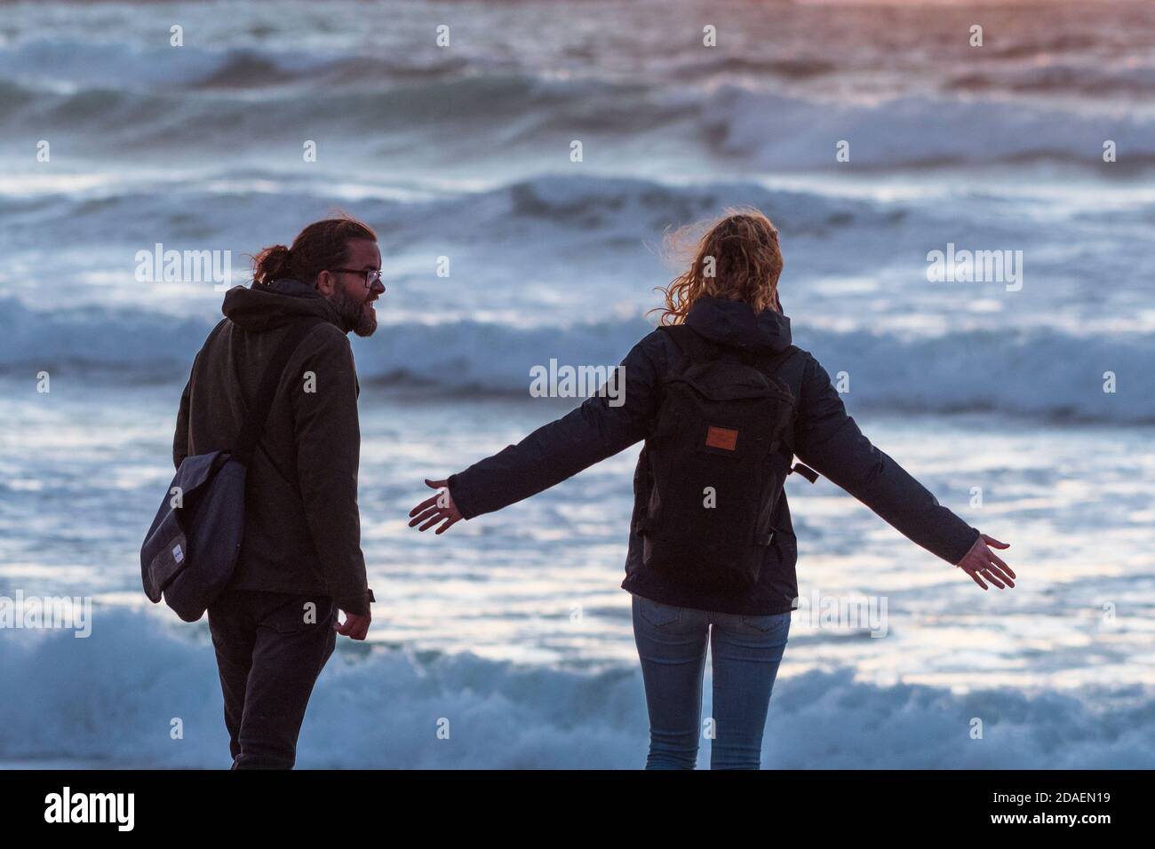 A couple of holidaymakers enjoying the evening light over Fistral Bay in Newquay in Cornwall. Stock Photo