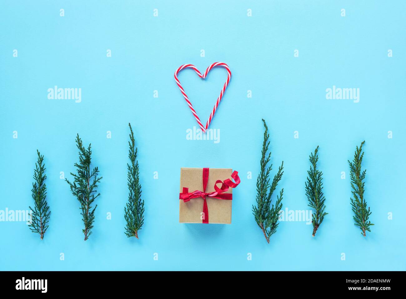 New Year's gift, cypress sprigs and a heart made of two candy canes on blue background. Christmas layout, flat lay, copy space. Stock Photo