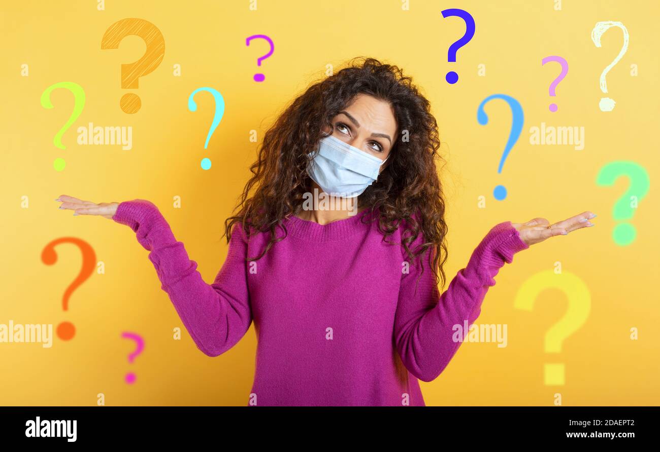 Girl with face mask has a lot of question about covid 19. Yellow background Stock Photo