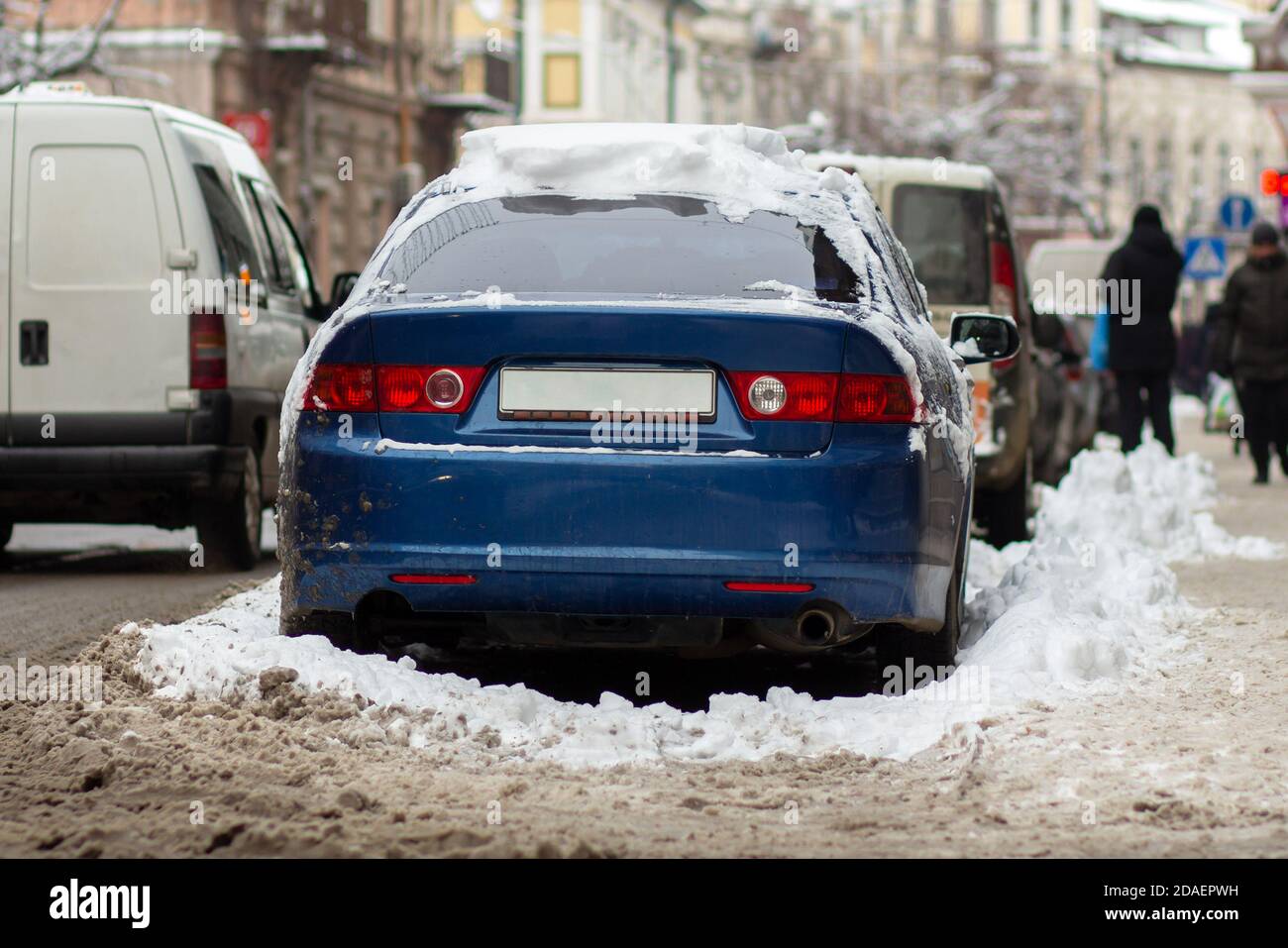 Cars parked on a side of city street covered with dirty snow in winter ...