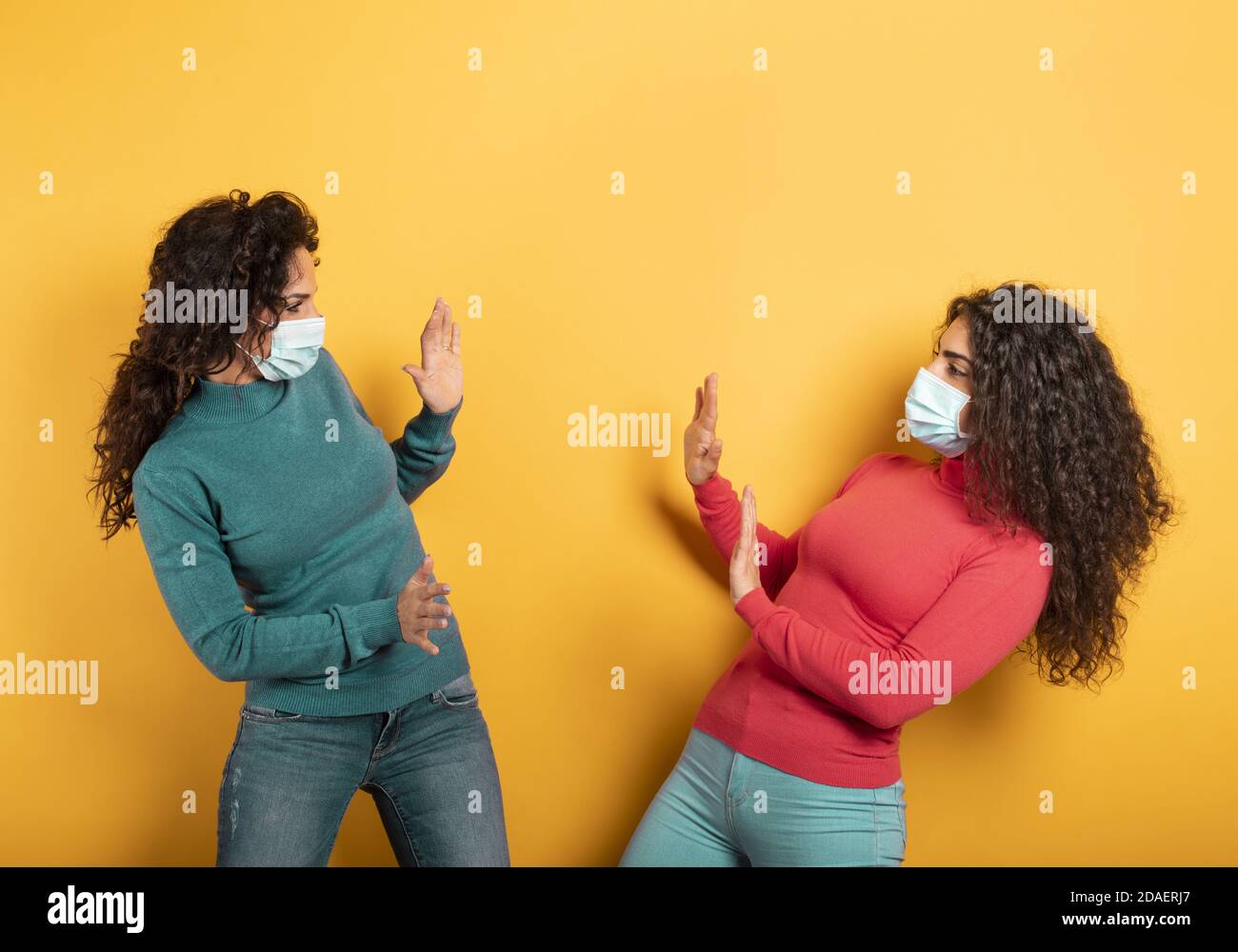 Friends stay away to avoid contact and contagion of the virus. Concept of codiv-19 rules to avoid pandemic. yellow background Stock Photo