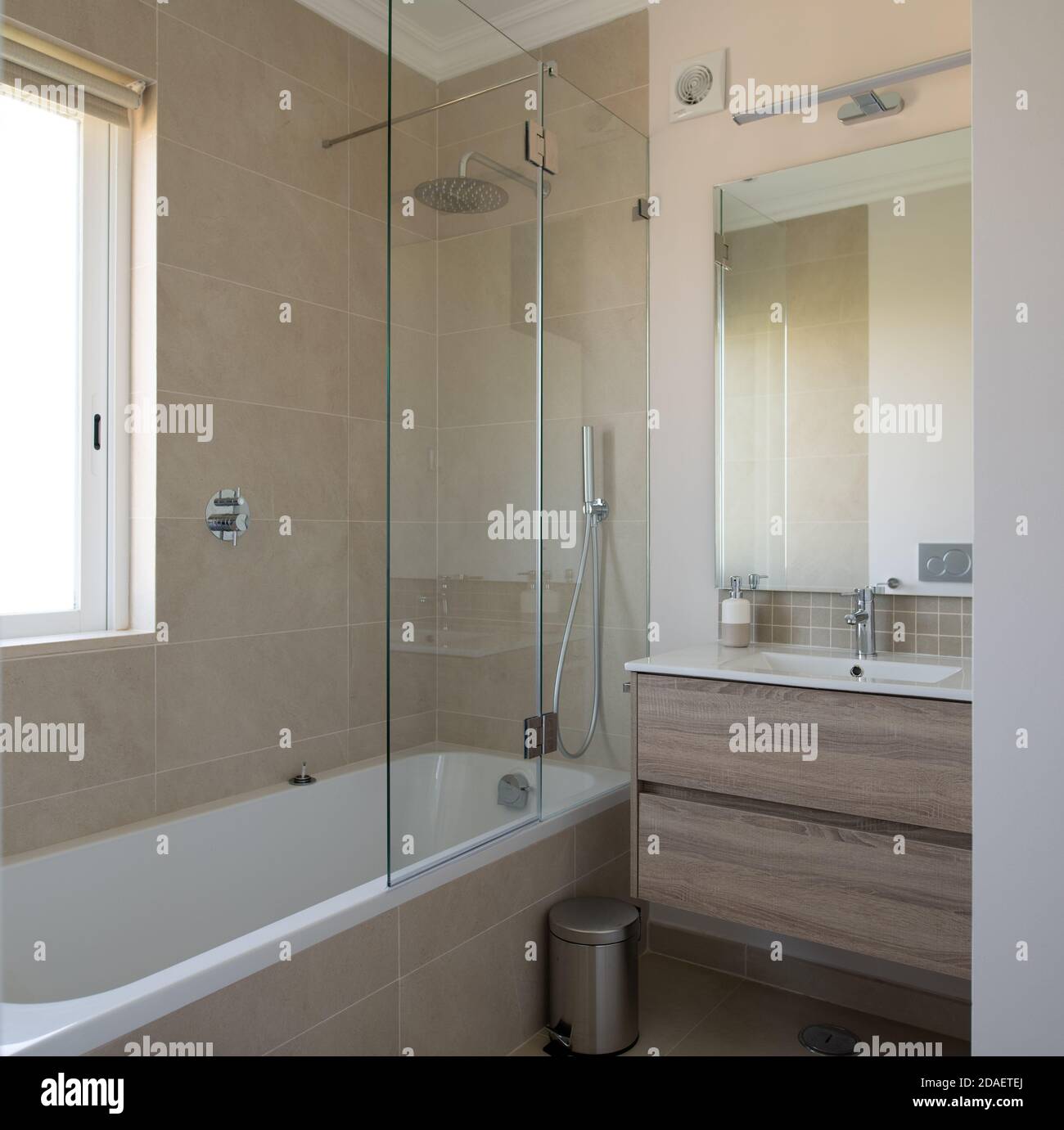 New bathroom with bath, sink and shower screen with beige tiled walls Stock Photo