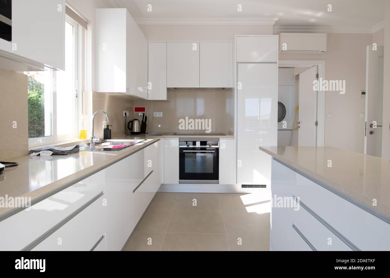 Brand new modern kitchen with white cabinets and beige stone counter top and ceramic tiled floor Stock Photo