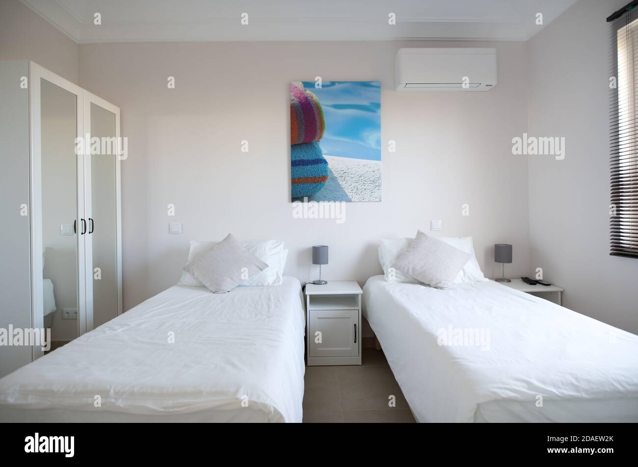 Clean twin bedroom in a house with white bed linen and white walls wardrobe with mirrored doors Stock Photo