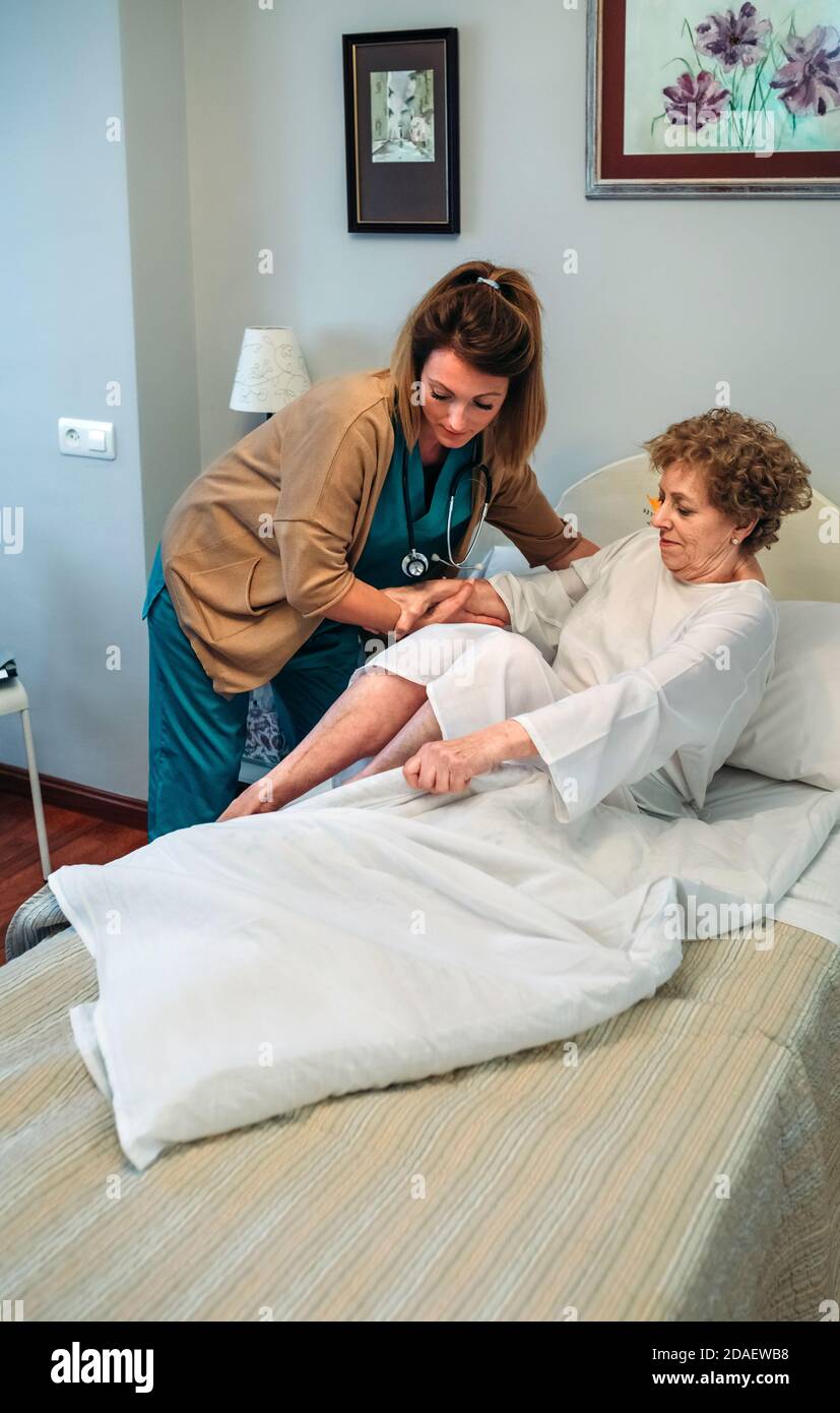 Caregiver helping elderly patient to get out of bed Stock Photo