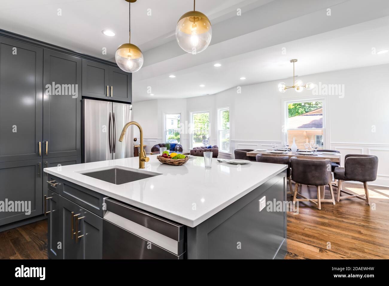 A luxurious white and grey kitchen with gold hardware and white marbled granite counter tops looking towards the dining room. Stock Photo
