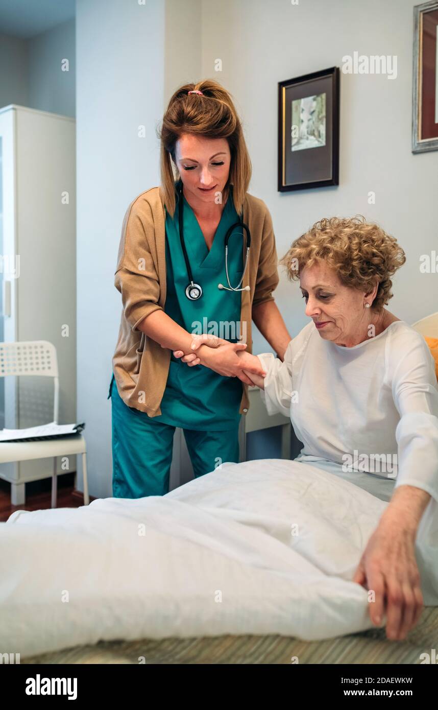 Caregiver helping elderly patient to get out of bed Stock Photo
