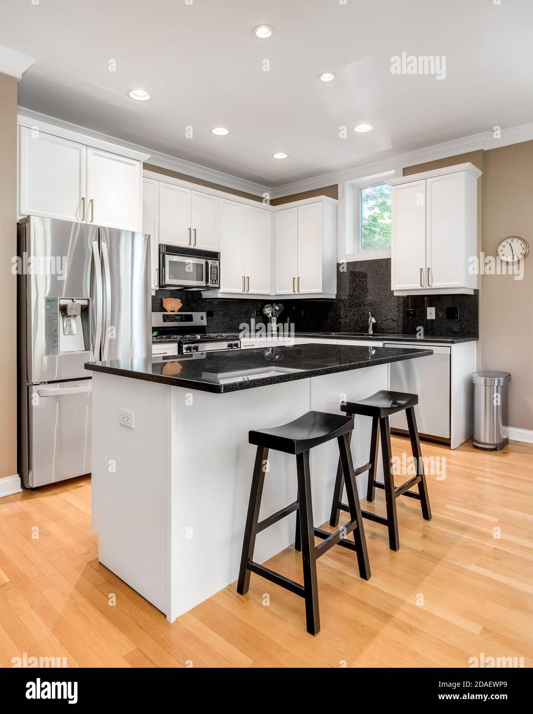 A white kitchen with a black granite counter top and back splash, stainless steel appliances, and hardwood floors. Stock Photo