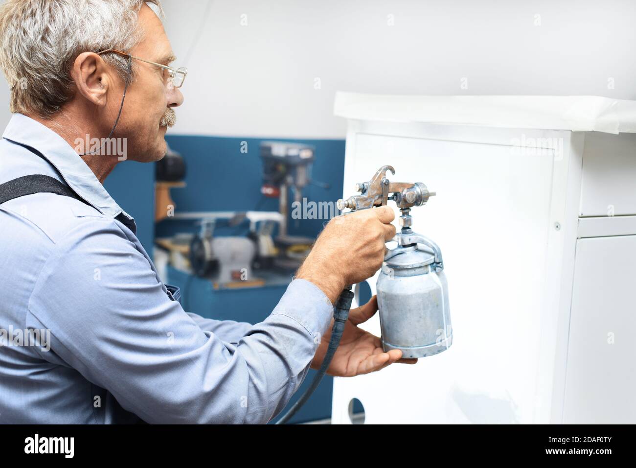 A pensioner with gray hair and glasses paints metal products. Additional earnings for an elderly person Stock Photo