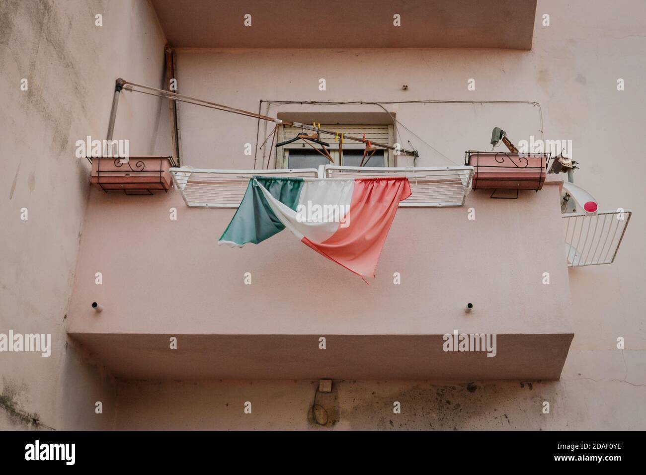 Weathered italian flag swings from the laundry rack on a balcony, seen on La Maddalena island, Sardinia, Italy. Stock Photo