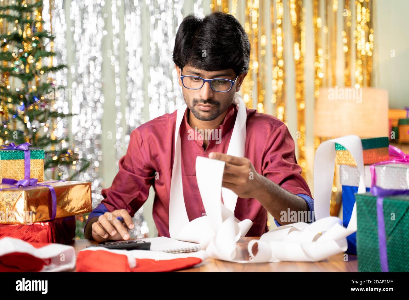 Young man busy in calculating holyday expenses after Christmas or new year 2021 holiday celebration showing with decorated background with gift in Stock Photo