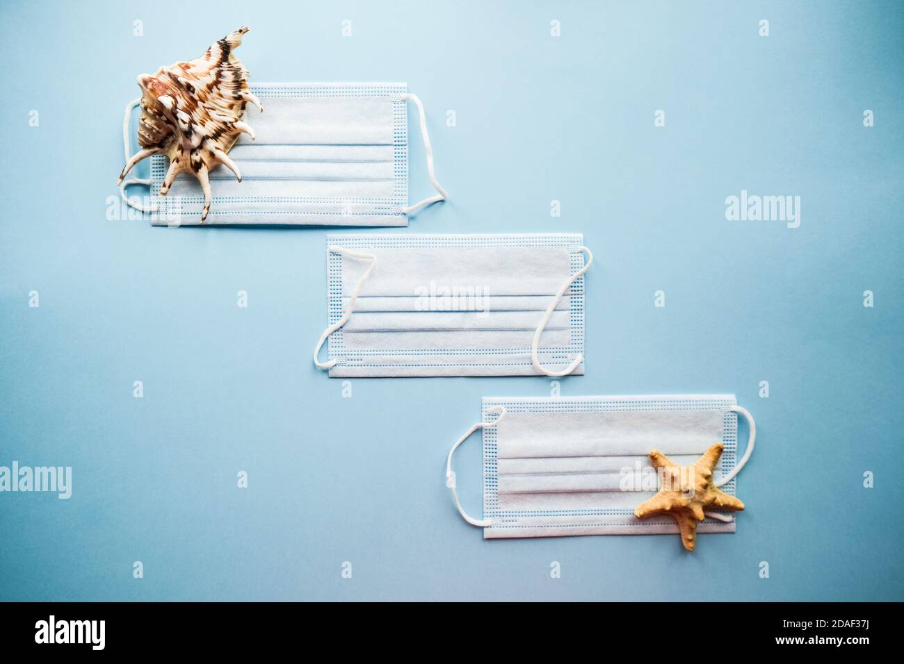 Medical masks and seashells on a blue background. Protection from COVID-19 concept. Flatlay. Top view. Stock Photo