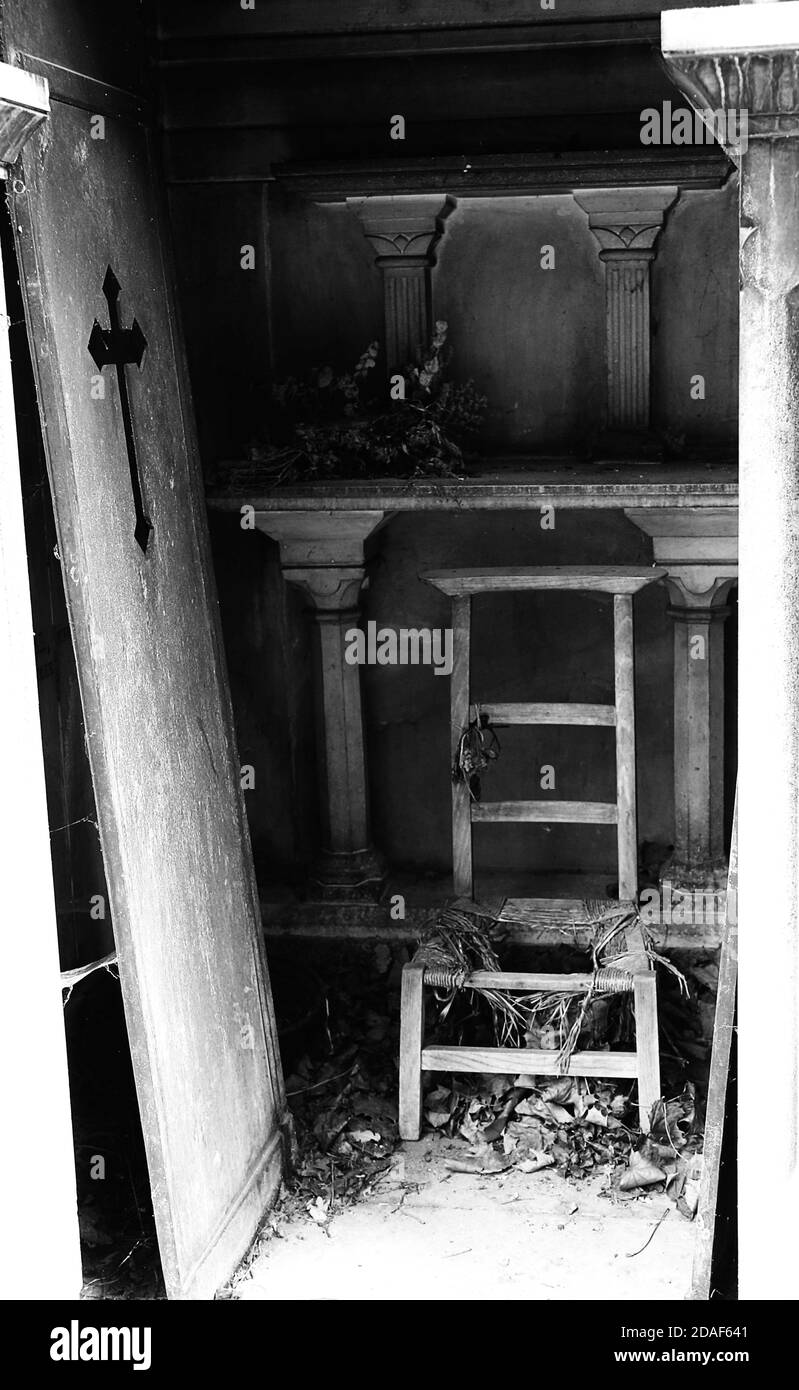 dramatic open grave with a serious old woman and the door torn up in an abandoned cemetery in black and white effect Stock Photo