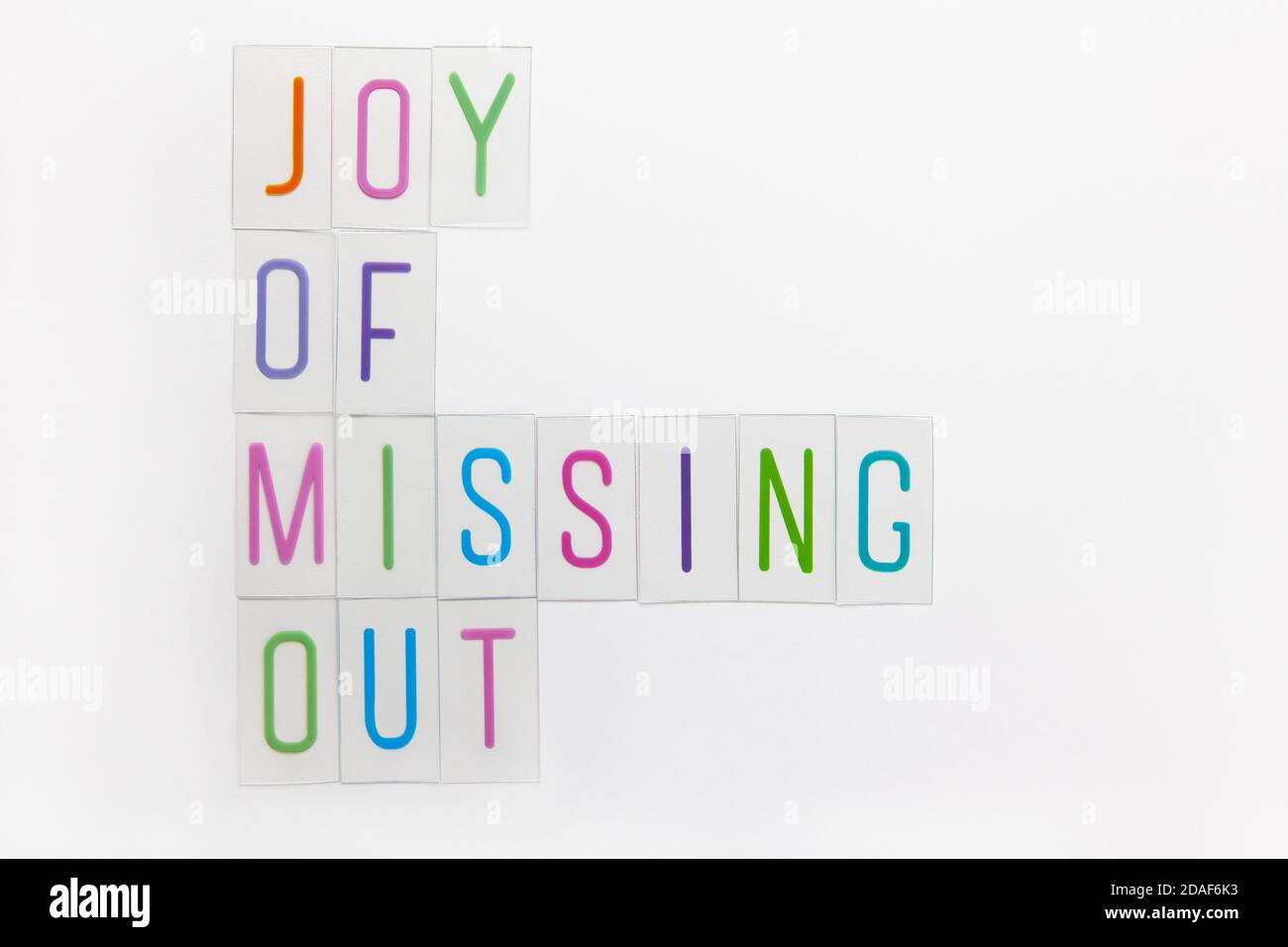 Abbreviation word JOMO, multicolored plastic letters on white background. JOMO - Joy Of Missing Out. Opposition, choice, social problem, digital detox Stock Photo