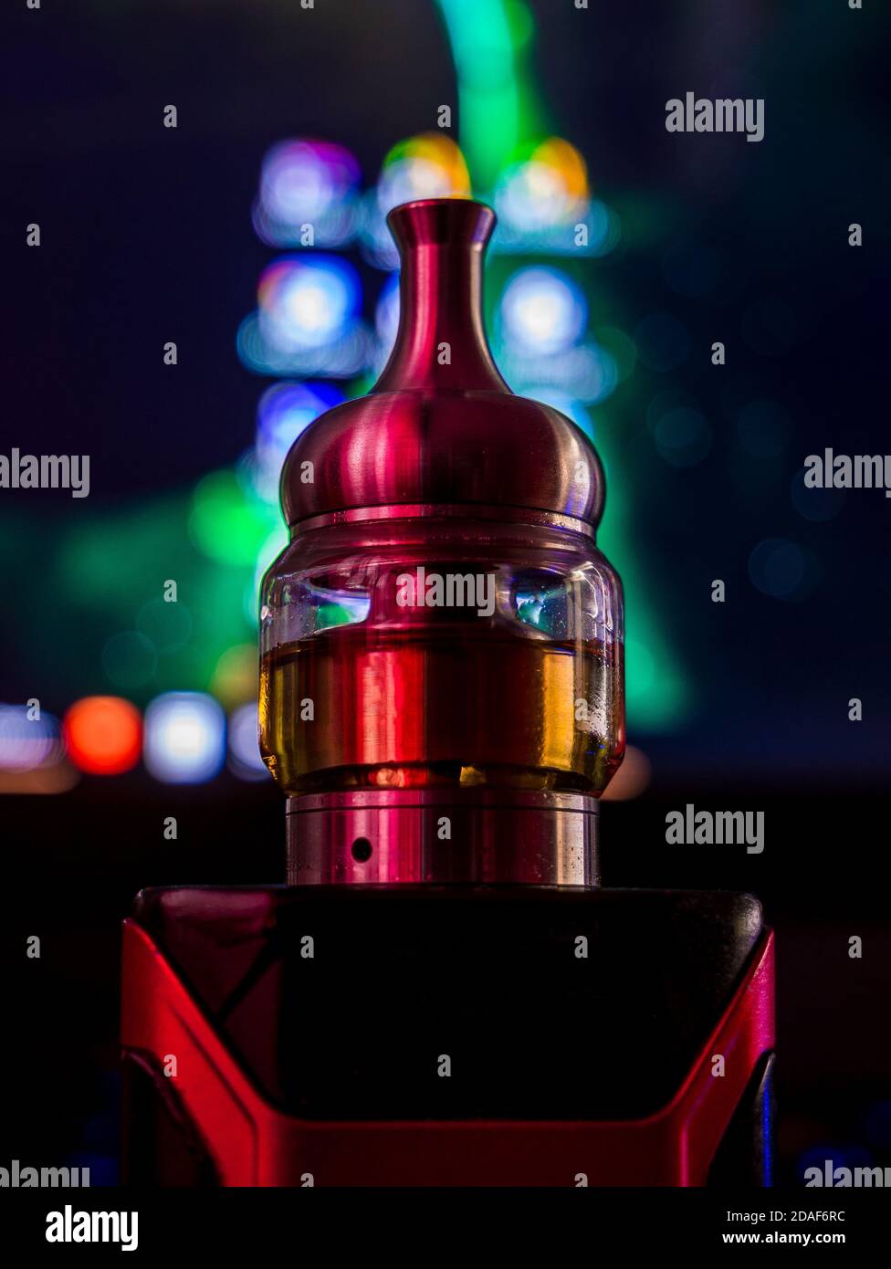 Filled electronic cigarette atomizer for vaping on top of the electronic mode. Unidentifiable multicolored blurred background. Stock Photo