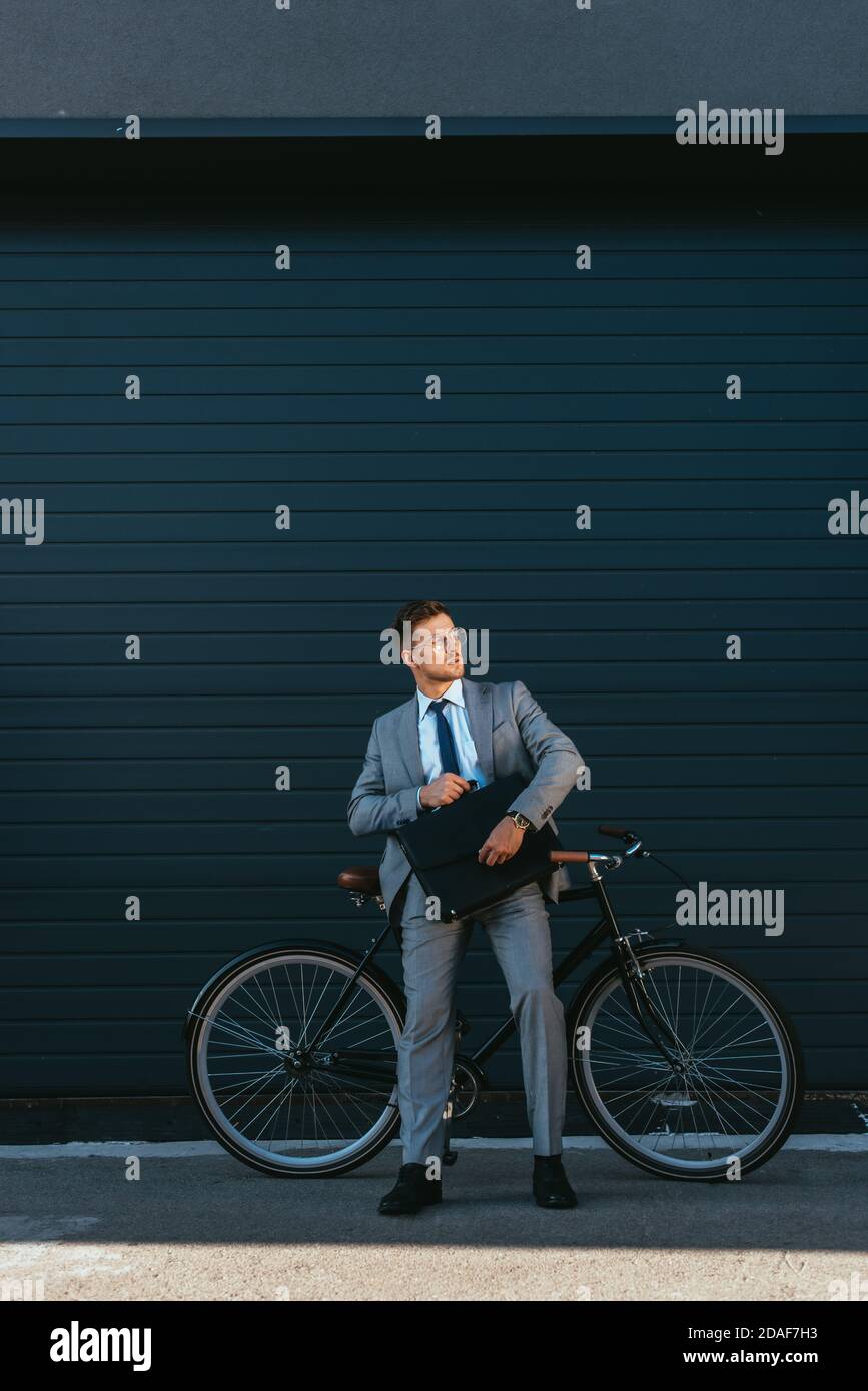 Young businessman holding briefcase while standing near bike and building Stock Photo