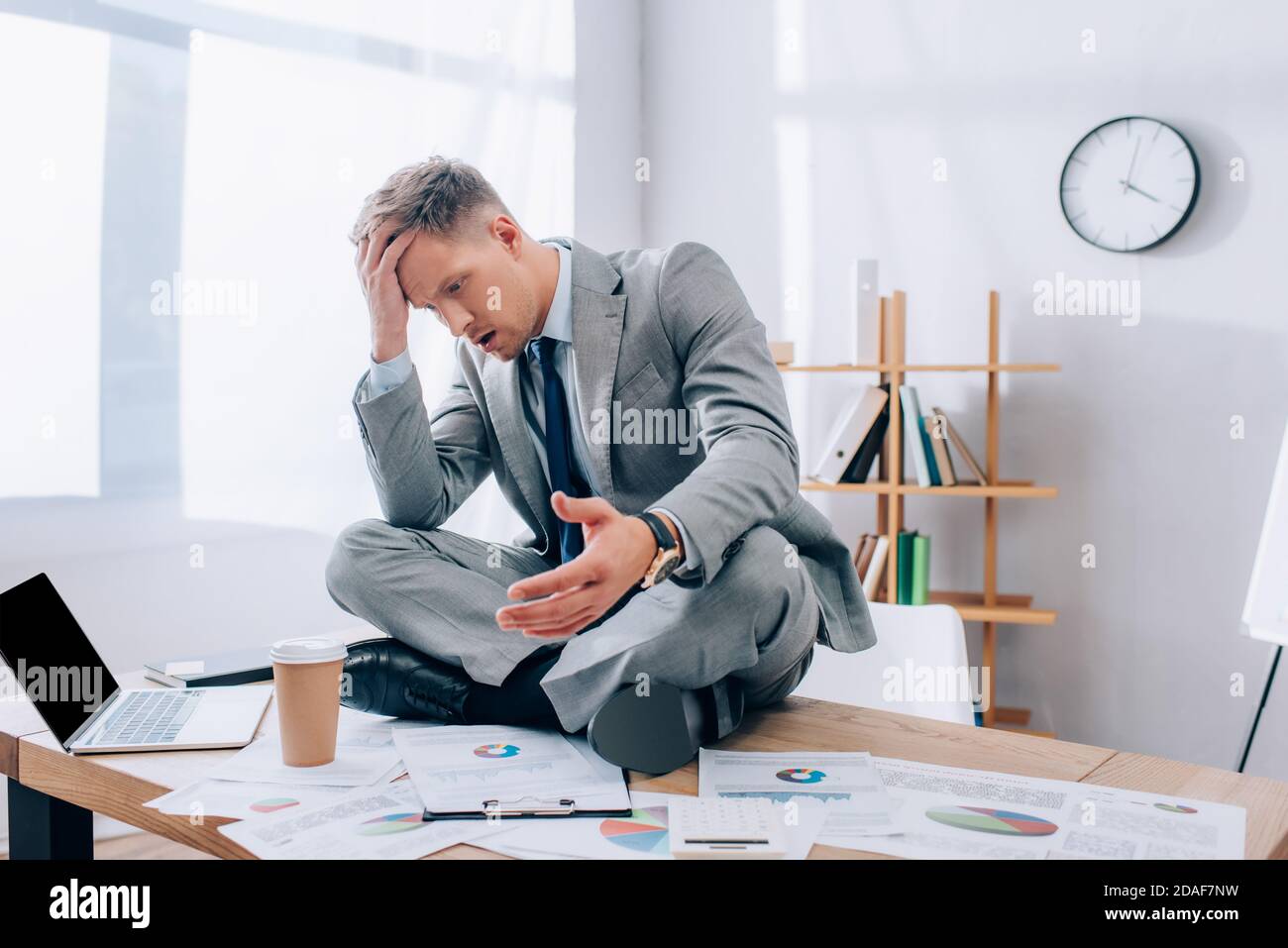 Thoughtful businessman sitting near laptop, papers and coffee to go on table in office Stock Photo