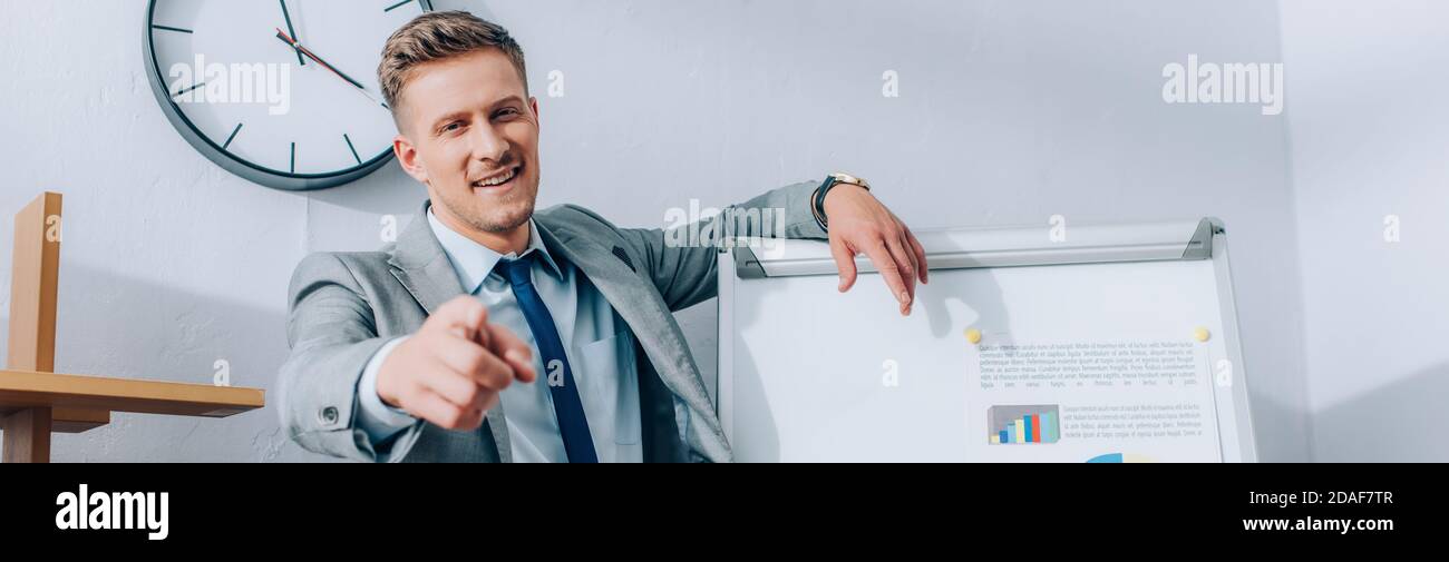 Pointing Near Positive businessman pointing with finger at camera near flipchart with ...