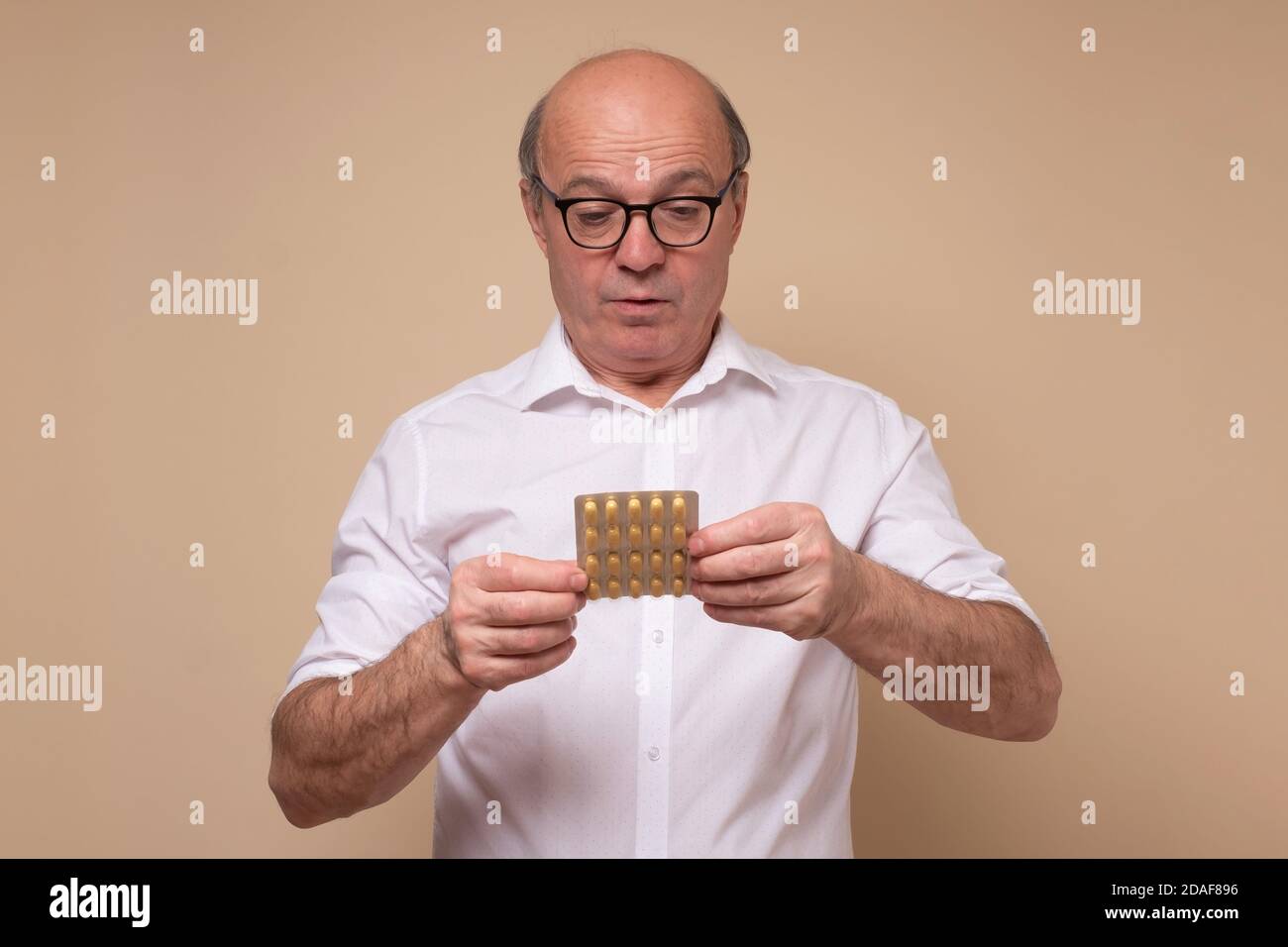 Puzzled caucasian senior man lookinb on pills Stock Photo