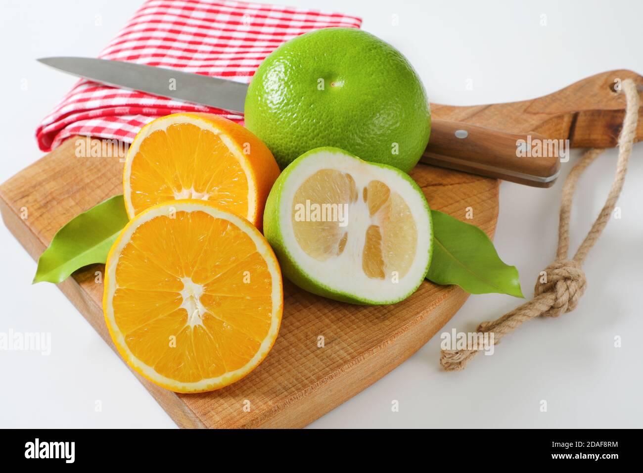 Still life of green grapefruits (sweetie, pomelit, oroblanco grapefruit) and halved orange with knife and tea towel on cutting board Stock Photo