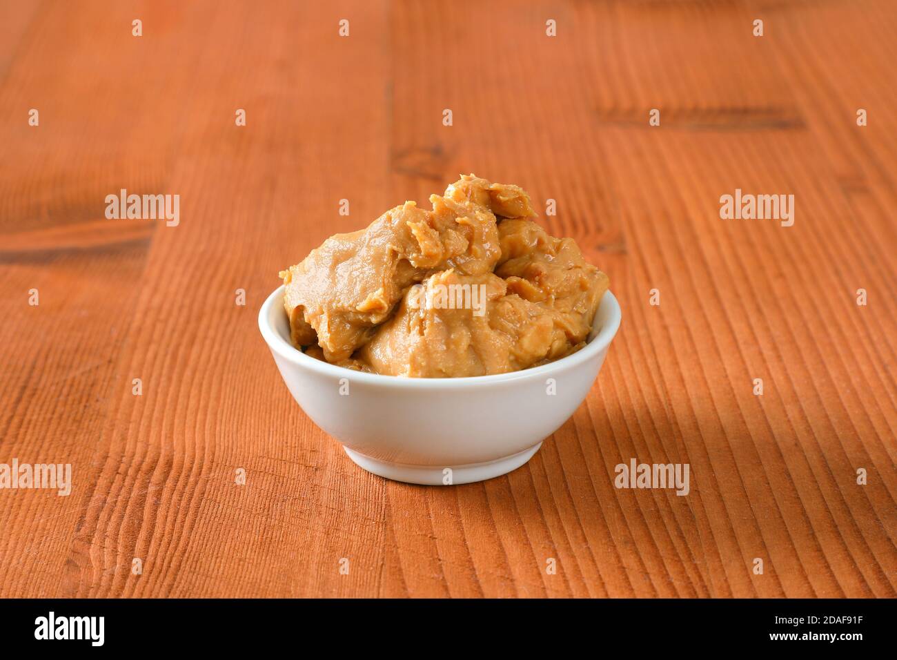 Crunchy peanut butter in white bowl on wooden background Stock Photo