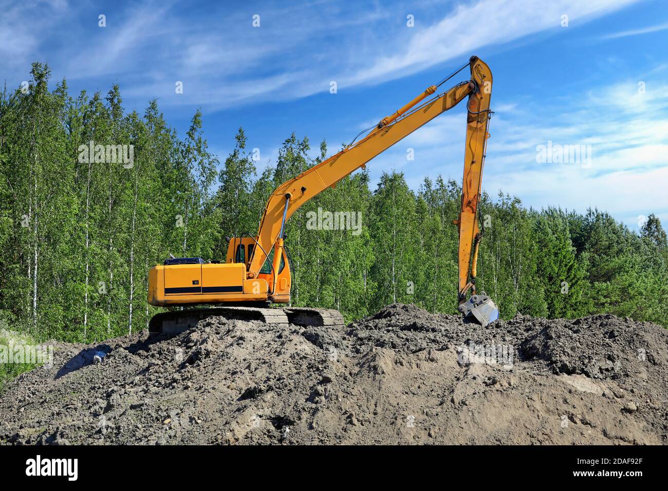 Yellow tracked excavator at work site on a heap of earth on a beautiful day of summer. Stock Photo