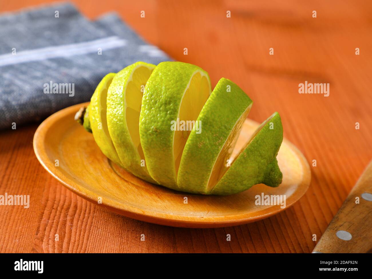 Lemon with green peel and yellow flesh, sliced on wooden plate Stock Photo