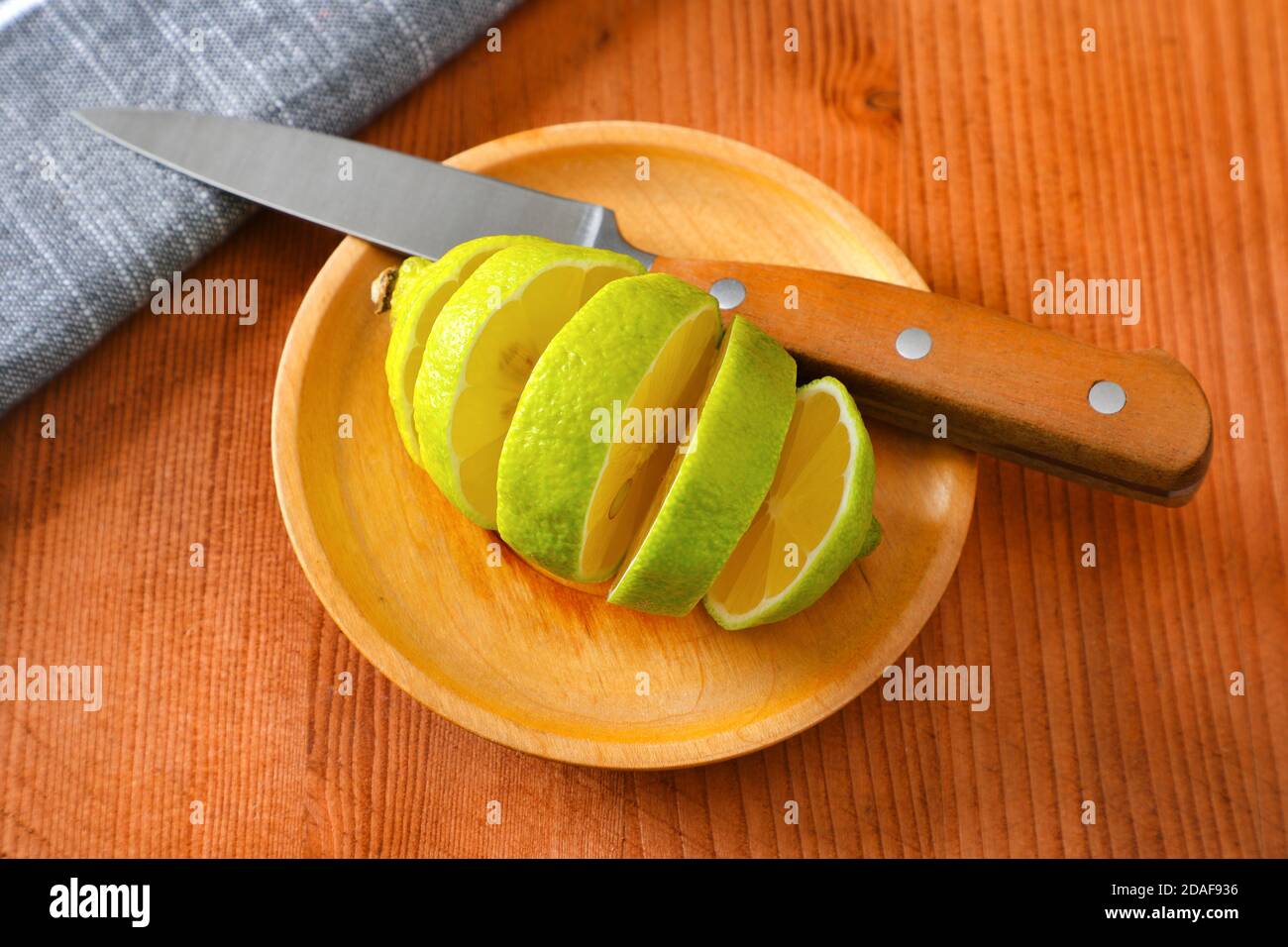 Lemon with green peel and yellow flesh, sliced on wooden plate Stock Photo
