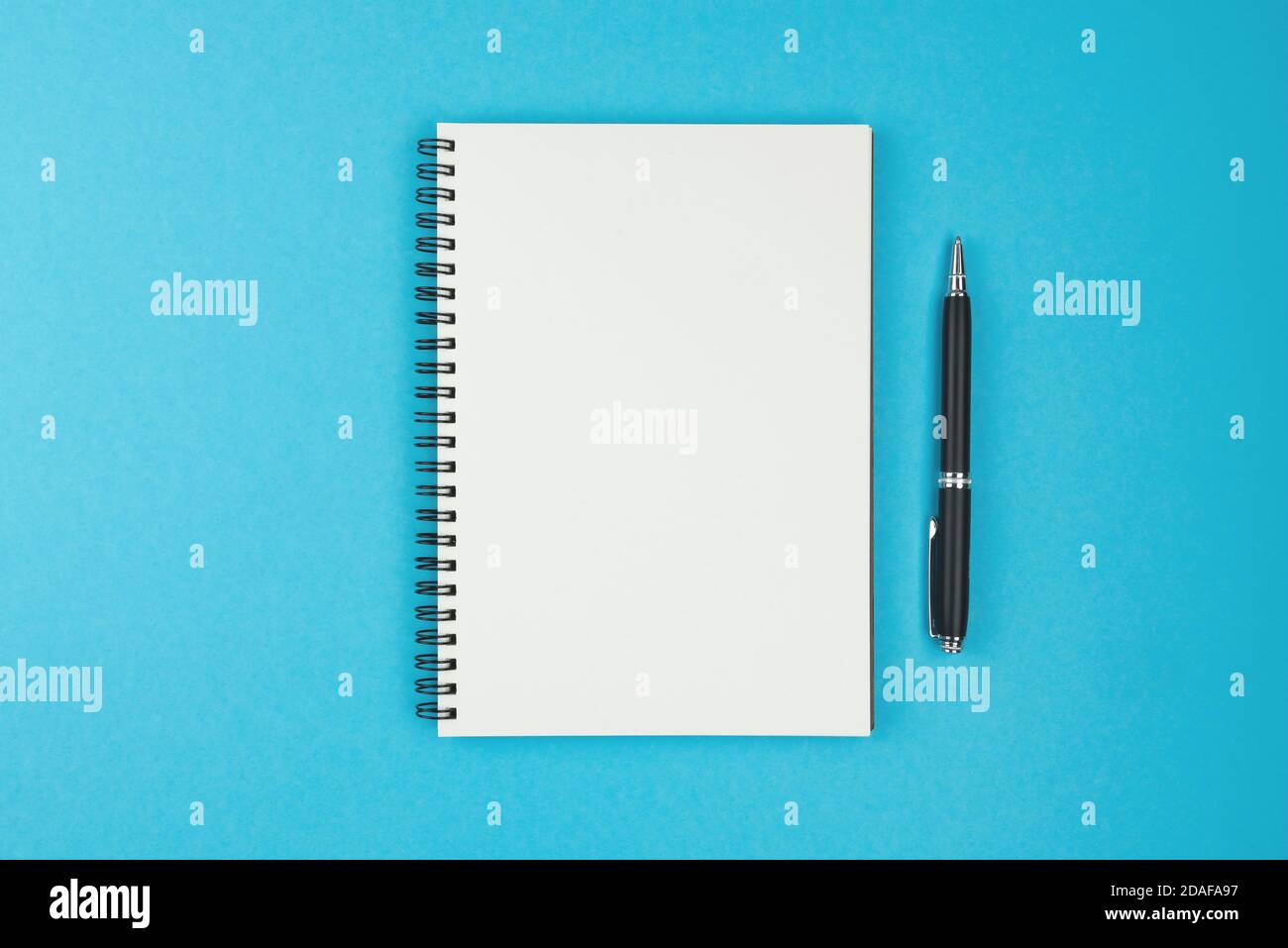 directly above view of blank spiral bound notebook and ballpoint pen on blue background Stock Photo