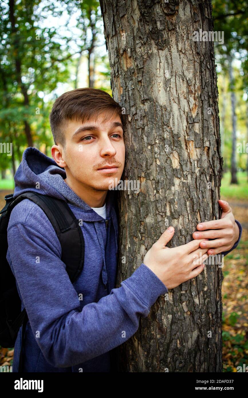 Young Man hug the Trunk of the Tree in the Forest Stock Photo