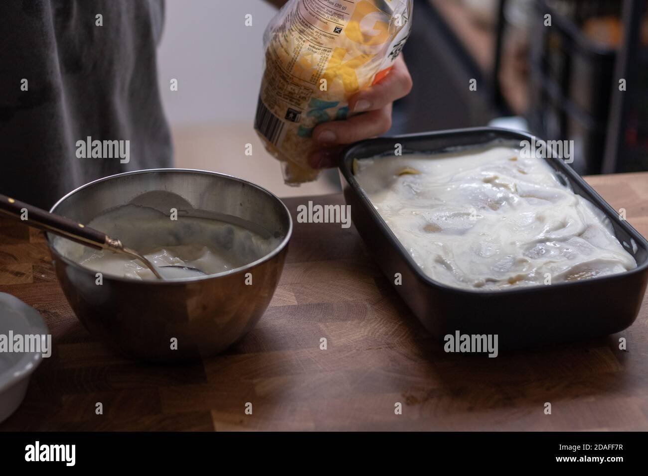 Preparing lasagne, hand pouring grated cheese Stock Photo