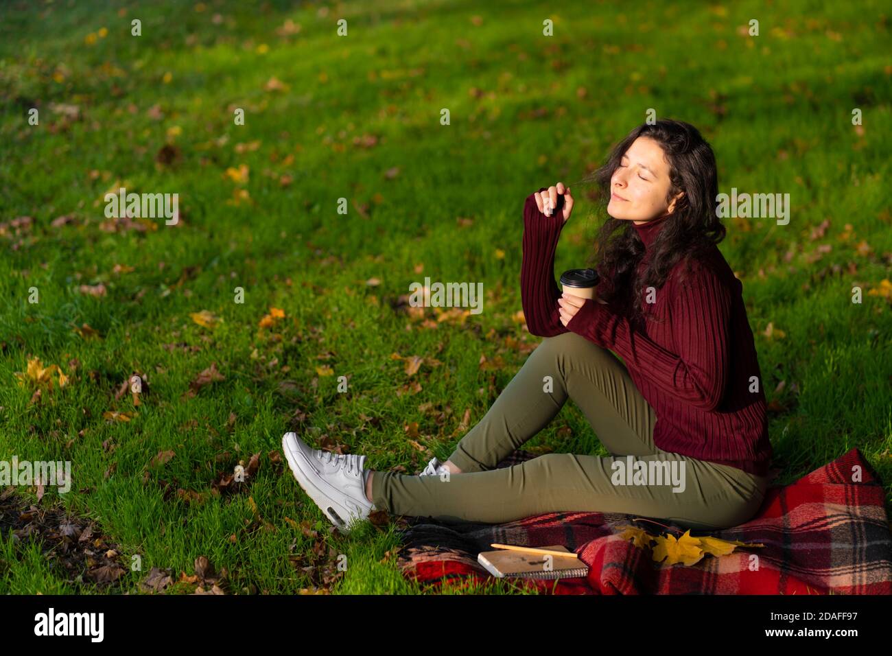 Pretty girl enjoys autumn and the beauty of nature sitting on a green ...