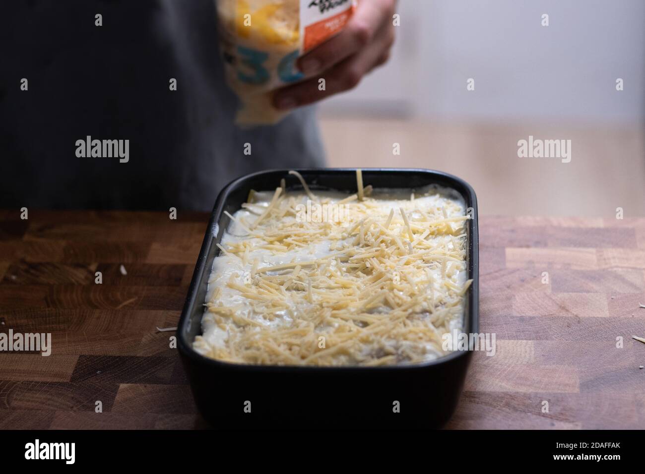 Preparing lasagne, hand pouring grated cheese Stock Photo