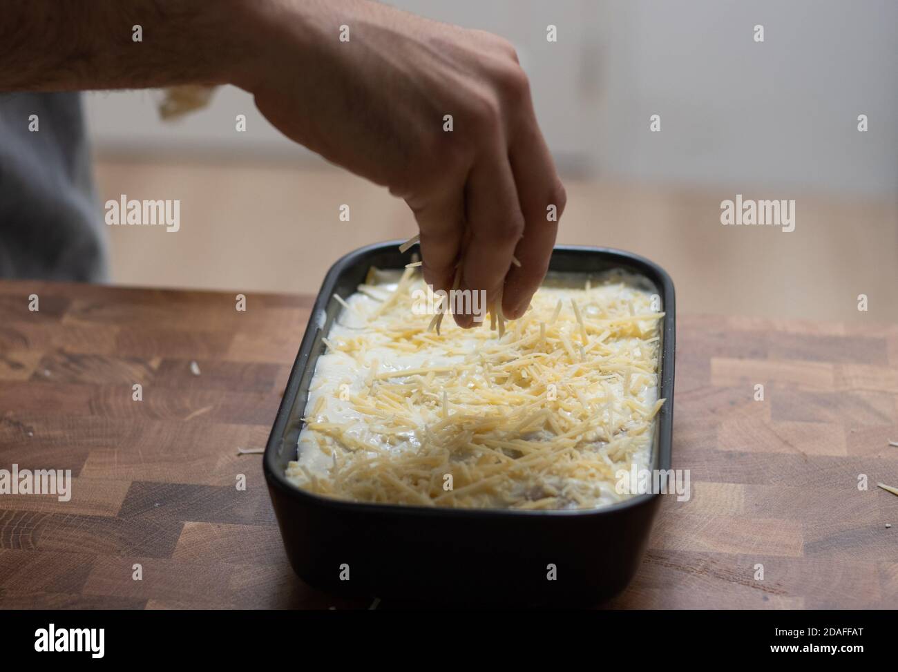 Preparing lasagne, hand pouring grated cheese Stock Photo