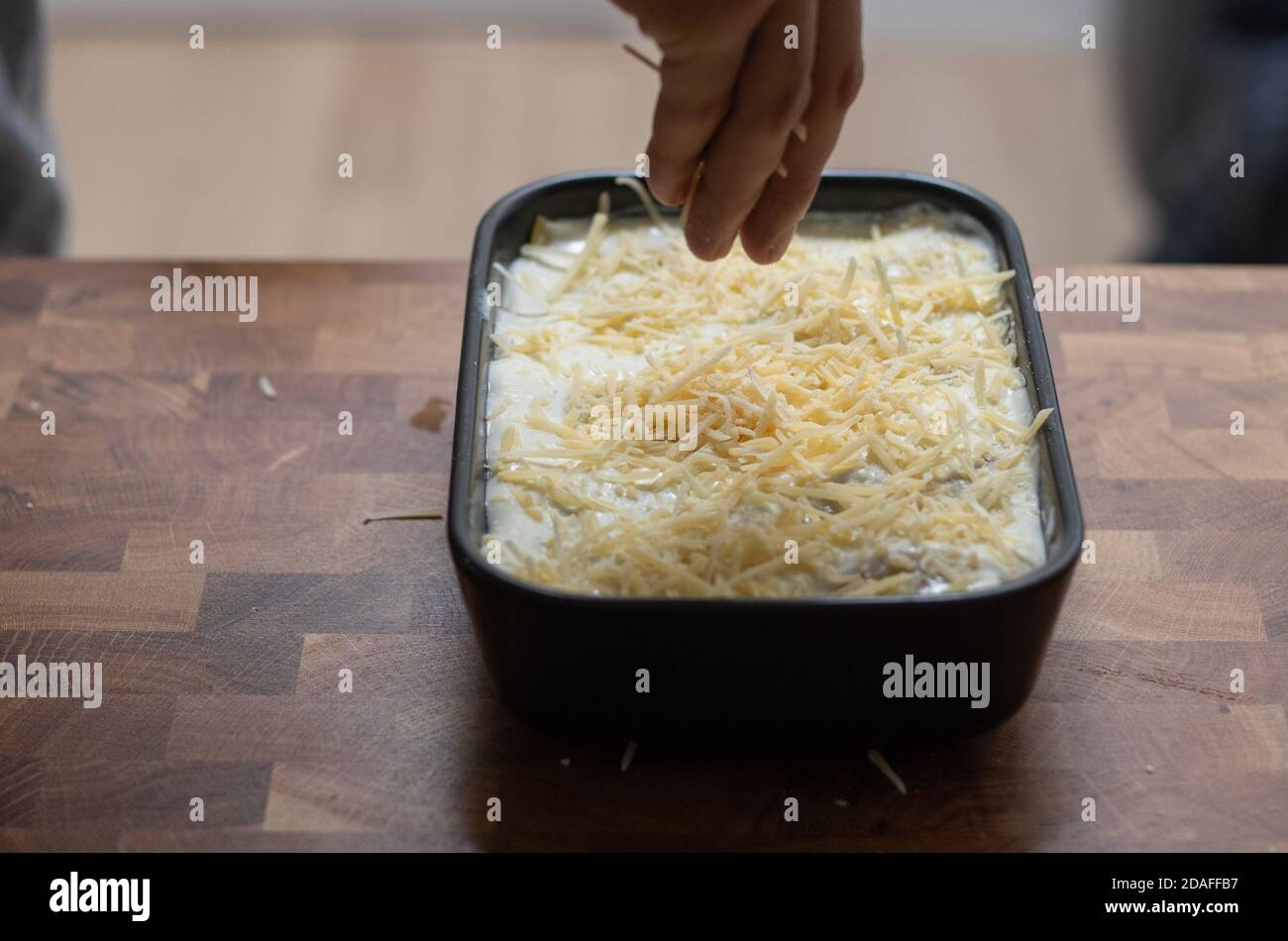 Preparing lasagne, hand pouring grated cheese Stock Photo