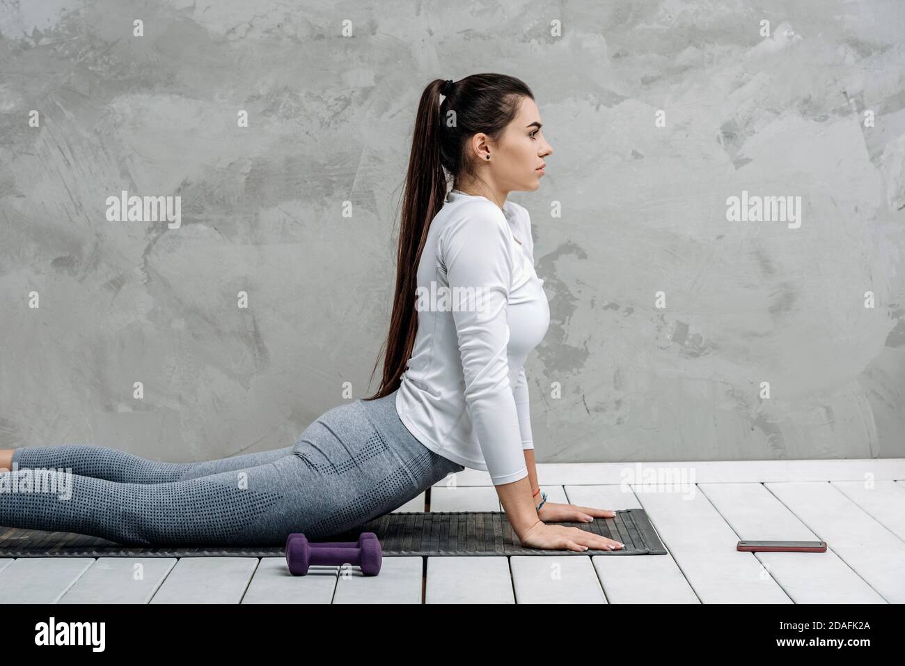 Young woman using smartphone during workout at home in the living room. Online personal trainer or on mobile phone. Workout online concept. Vintage co Stock Photo