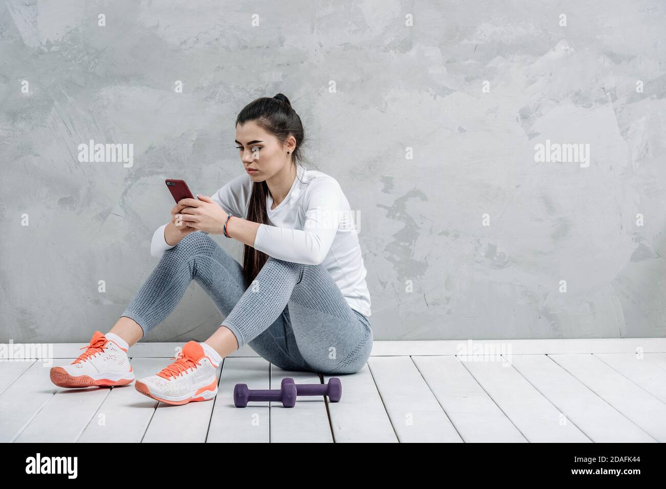 Young woman using smartphone during workout at home in the living room. Online personal trainer or on mobile phone. Workout online concept. Vintage co Stock Photo