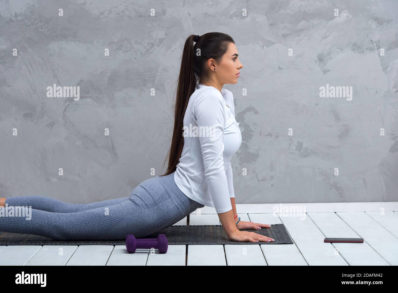 Young woman using smartphone during workout at home in the living room. Online personal trainer or on mobile phone. Workout online concept Stock Photo
