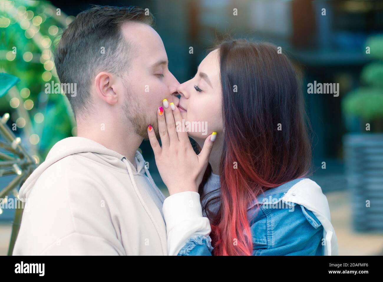 A young happy couple in love touch their lips in a tender kiss outside on a summer afternoon. Stock Photo