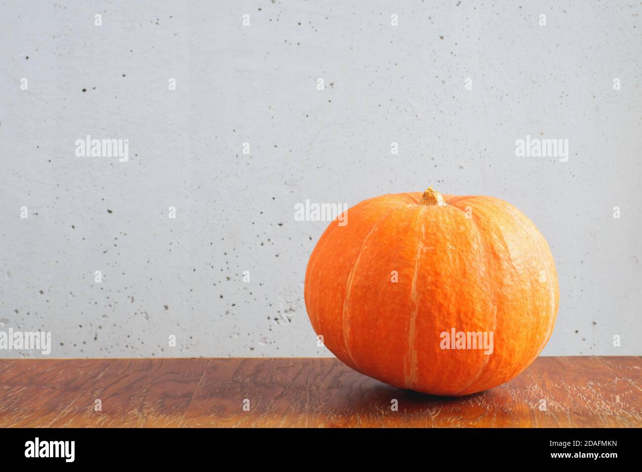 Orange pumpkin on a brown wooden table and against a gray concrete wall ...
