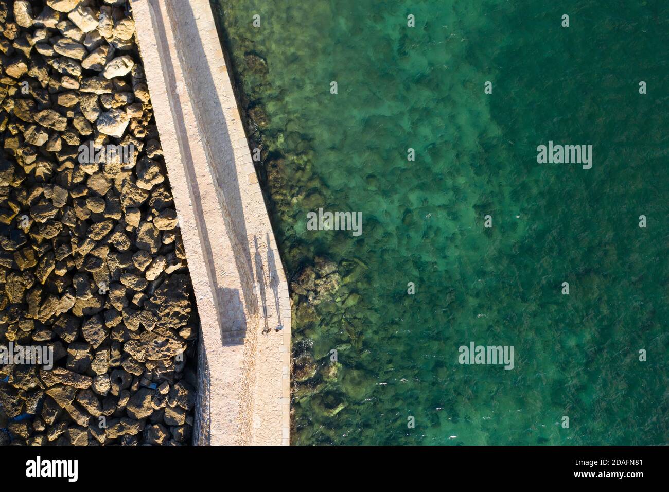 Aerial view of two people casting long shadows on the walkway to the lighthouse in the city of Chania, Crete, Greece Stock Photo