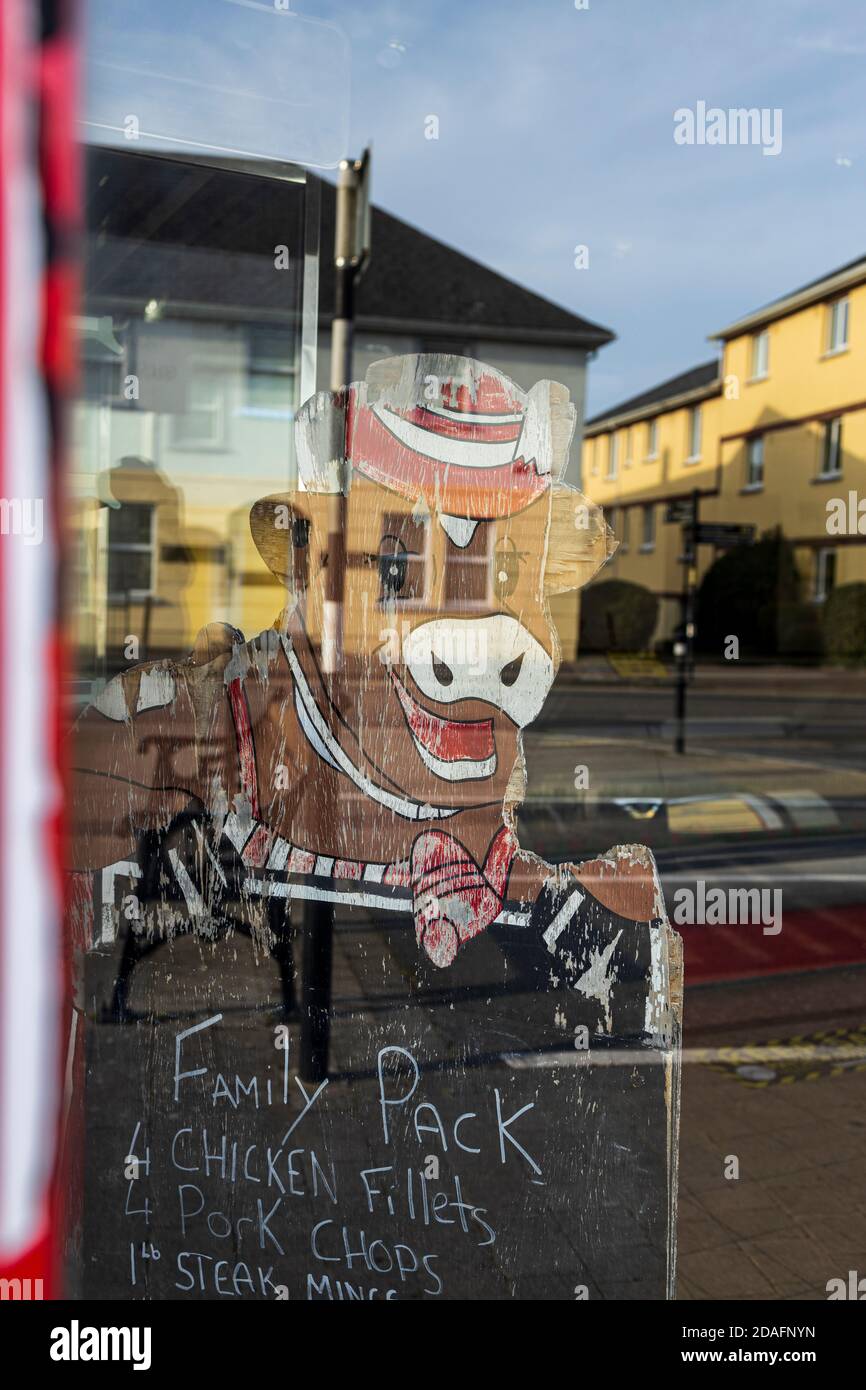 Laughing cow blackboard behind the closed door of a butchers shop advertising a family pack of meats, with reflections of houses in the glass, County Stock Photo