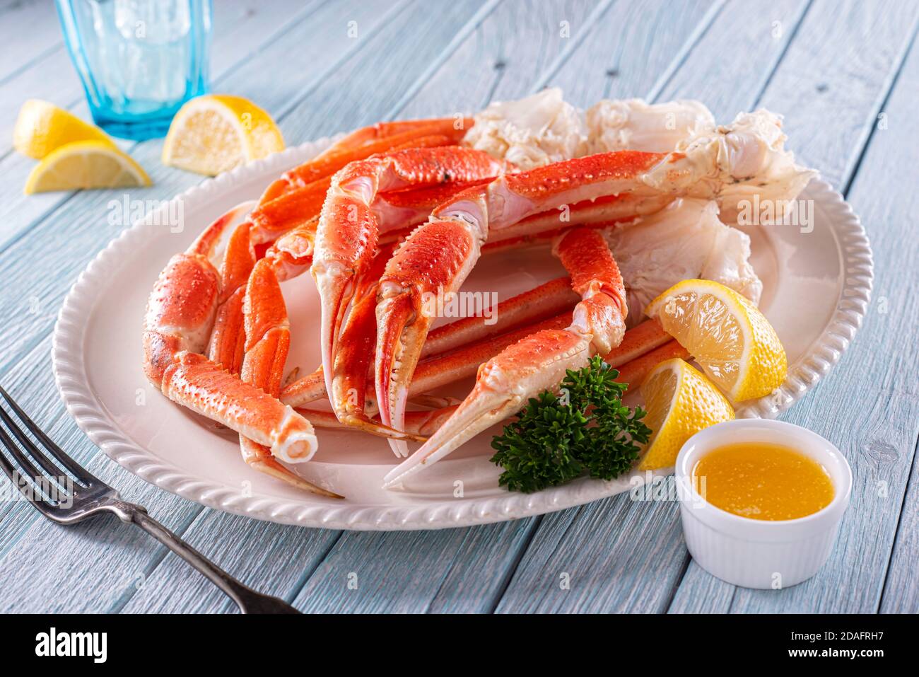 A plate of delicious snow crab leg clusters with lemon, parsley and melted butter. Stock Photo